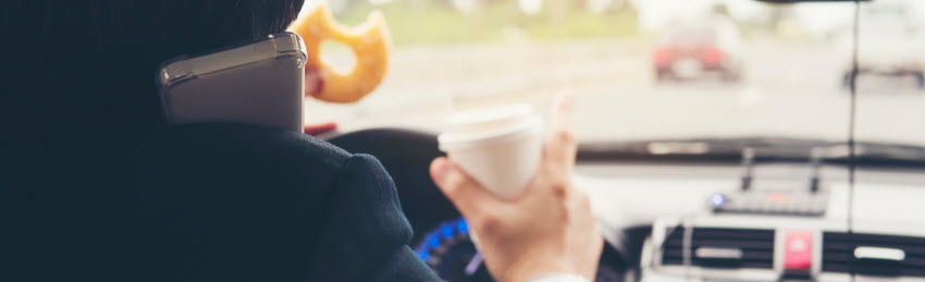 man driving while hold donut phone and coffee cup